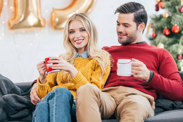 couple holding christmas coffee cups and resting at home together - Φωτογραφία, εικόνα