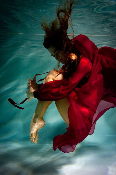 Dancing woman under the water in a pool in a red dress. - Foto, imagen