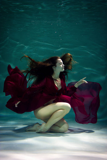 Dancing woman under the water in a pool in a red dress. - Φωτογραφία, εικόνα