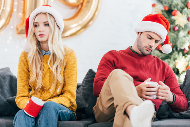 coppia sconvolta in cattivo umore tenendo tazze di caffè e seduto a casa la vigilia di Natale
 - Foto, immagini