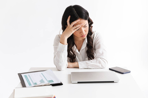 Image of upset or tired asian business woman 20s wearing office clothing sitting at table with laptop and grabbing head isolated over white background - Foto, Bild