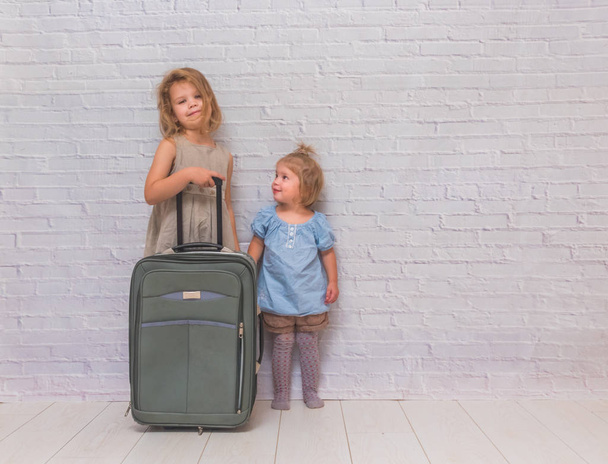 a two girls, kids with suitcase on wheels on white brick wall background - Photo, Image