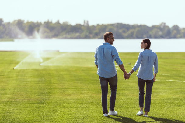 couple in sunglasses holding hands and looking at each other at lawn outdoors  - Photo, Image