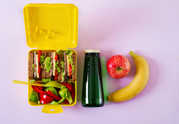 Boîte à lunch scolaire saine avec sandwich au bœuf et légumes frais, bouteille d'eau et fruits sur fond rose. Vue de dessus. Pose plate
 - Photo, image