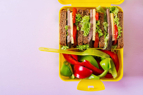Здорова шкільна обідня коробка з яловичим бутербродом та свіжими овочами на рожевому фоні. Вид зверху. Плоский прошарок
 - Фото, зображення