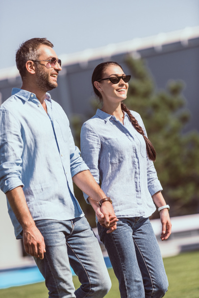 happy couple in sunglasses holding hands and walking outdoors  - Fotó, kép