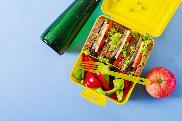 Boîte à lunch scolaire saine avec sandwich au bœuf et légumes frais, bouteille d'eau et fruits sur fond bleu. Vue de dessus. Pose plate
 - Photo, image
