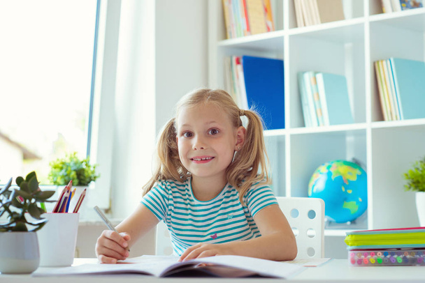 Portrait of pretty schoolgirl at classroom writing at the table - Zdjęcie, obraz