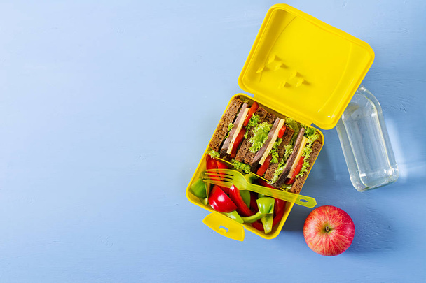 gesunde Schulessenbox mit Rindfleischsandwich und frischem Gemüse, Flasche Wasser und Obst auf blauem Hintergrund. Ansicht von oben. flache Lage - Foto, Bild