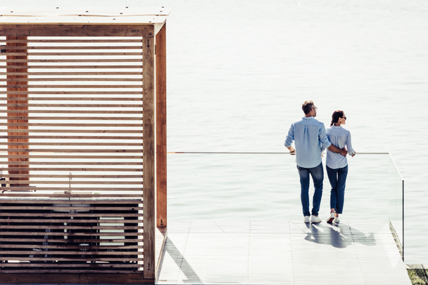 high angle view of stylish couple standing on pier near lake at country house  - Photo, Image