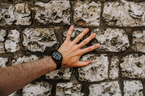 wykadrowanego obrazu męskiej ręki sobie zegarek na rękę i dotykając ukamienowany ściana budynku  - Zdjęcie, obraz