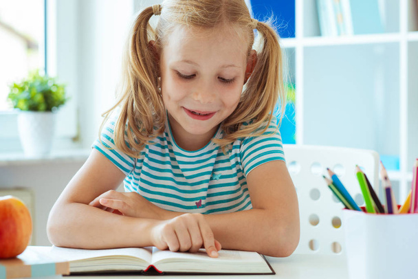 Portrait of a cute little girl read book at the table in light classroom  - Fotoğraf, Görsel