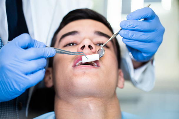 Young attractive man receiving a dental treatment. Close up shot. - Photo, image