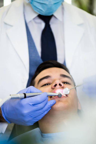 Young attractive man receiving a dental treatment. Close up shot. - Foto, afbeelding