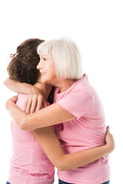 Widok z boku młodych i starszych kobiet w kolorze różowym t-shirty, przytulanie na białym tle na biały, koncepcja świadomości raka piersi  - Zdjęcie, obraz