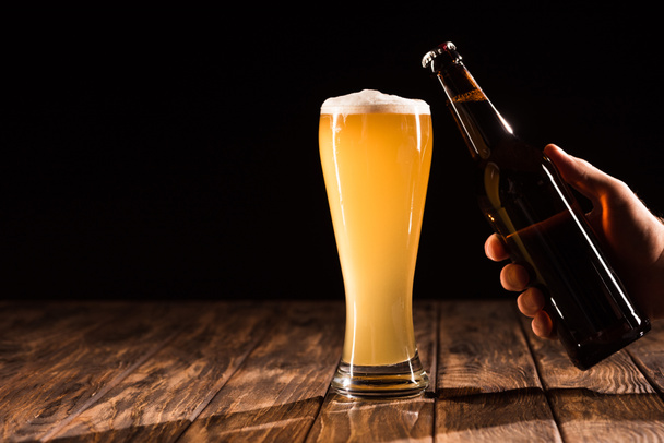 vista parcial del hombre tintineo botella de cerveza con taza de cerveza fresca en la mesa de madera
  - Foto, Imagen