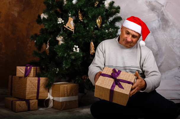 abuelo sentado cerca del árbol de Navidad con caja de regalo
 - Foto, imagen