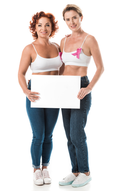 women in bras with breast cancer awareness ribbons holding blank card and smiling at camera isolated on white  - Foto, imagen