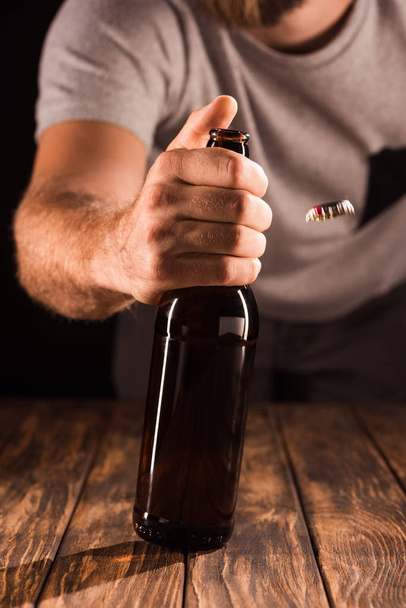 Μερική άποψη του ανθρώπου άνοιγμα μπουκάλι μπύρα στο ξύλινο τραπέζι  - Φωτογραφία, εικόνα