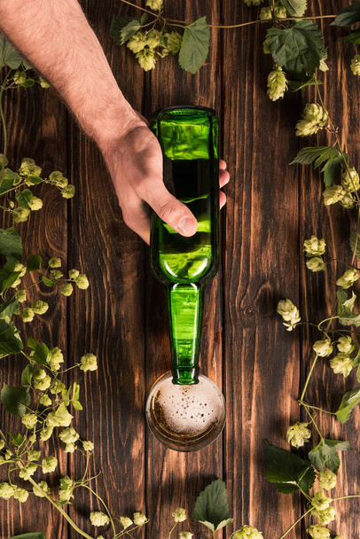 cropped image of man pouring beer into glass at wooden table with hop  - Fotoğraf, Görsel