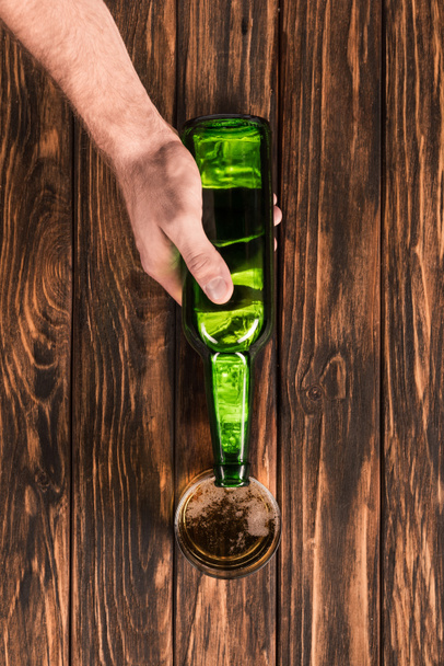木製のテーブルにグラスにビールを注ぐ男の部分的なビュー  - 写真・画像