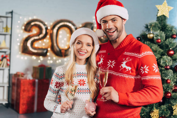 casal sorrindo com taças de champanhe segurando porquinho banco com poupança para o ano novo
 - Foto, Imagem
