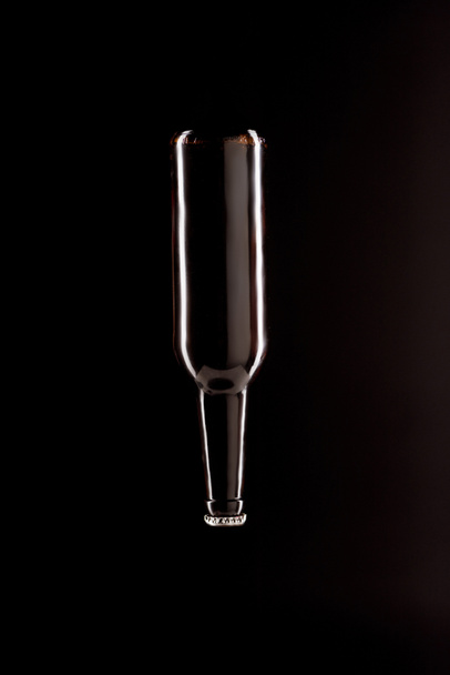 bierfles ondersteboven geïsoleerd op zwarte achtergrond, minimalistische concept - Foto, afbeelding