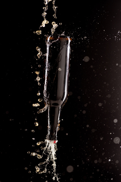 selective focus of beer pouring on bottle upside down with splashes around isolated on black background  - Φωτογραφία, εικόνα