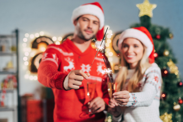 messa a fuoco selettiva di coppia in cappelli di Babbo Natale che tengono scintille a Natale
 - Foto, immagini