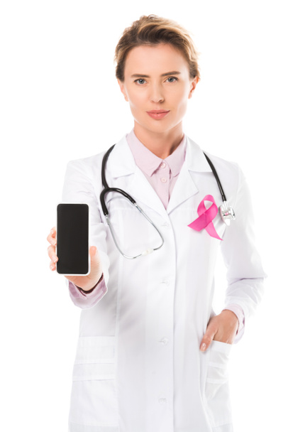 Doktor smartphone boş ekran ile tutarak ve kameraya bakarak pembe kurdele ile beyaz, meme kanseri bilinçlendirme kavramı üzerinde izole   - Fotoğraf, Görsel
