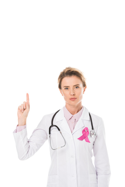 doctor with pink ribbon pointing up with finger and looking at camera isolated on white, breast cancer awareness concept  - Foto, afbeelding