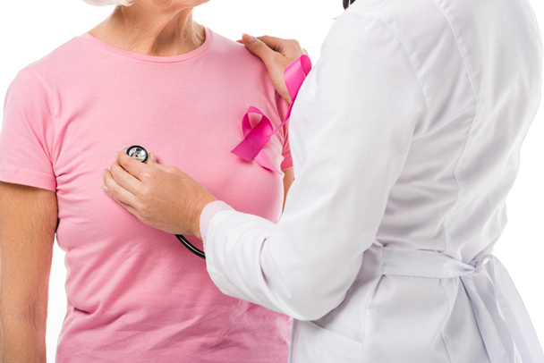 bijgesneden schot van arts met de stethoscoop controle van de gezondheid van de vrouw van de senior met borst kanker bewustzijn lint geïsoleerd op wit - Foto, afbeelding
