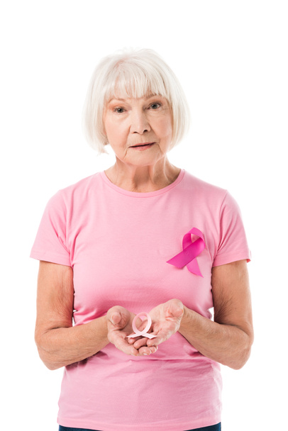mulher sênior segurando fita rosa e olhando para câmera isolada em branco, conceito de câncer de mama
 - Foto, Imagem