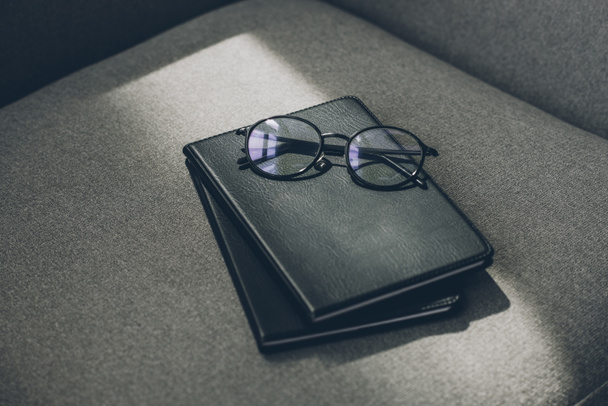 eyeglasses and two notebooks on grey armchair in office - Фото, зображення
