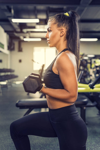 Full length portrait of young slim woman doing lunges with dumbbells in the gym. Biceps training - Foto, Imagem