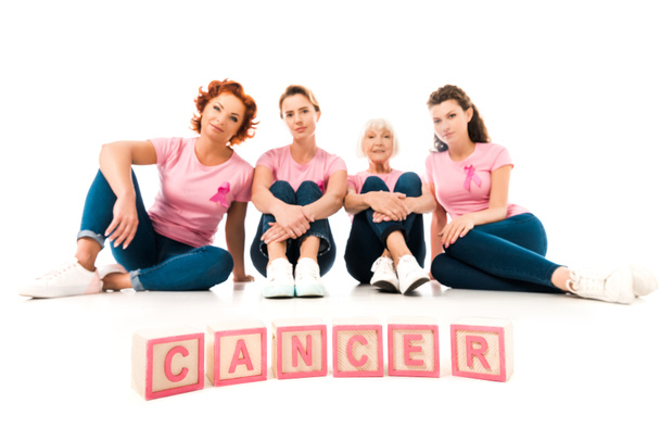 γυναικών ροζ μπλουζάκια κάθεται και βλέπει κάμερα, λέξη καρκίνος απομονωθεί σε λευκό - Φωτογραφία, εικόνα