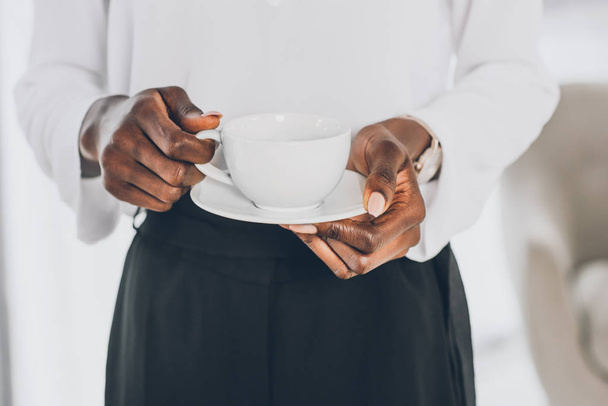 περικομμένη εικόνα κομψή Αφρικανικός Αμερικανός επιχειρηματίας κρατώντας κούπα καφέ στο γραφείο - Φωτογραφία, εικόνα