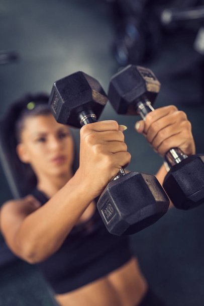 Concentrated woman lifting dumbbells in gym - Photo, image