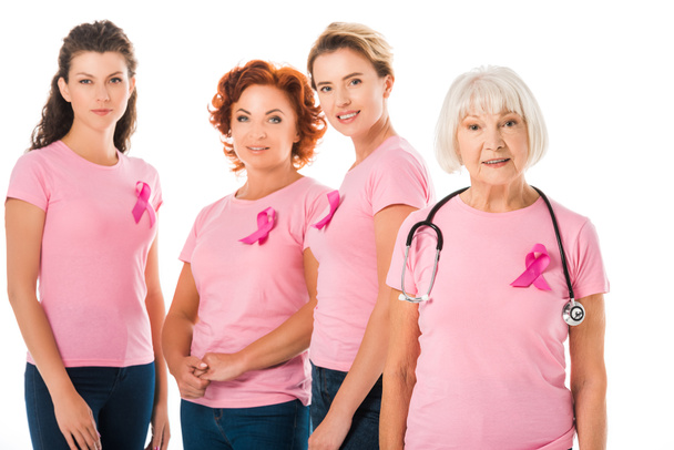 Frauen in rosafarbenen T-Shirts mit Brustkrebs-Aufklärungsbändern und Oberärztin mit Stethoskop lächeln vereinzelt in die Kamera - Foto, Bild