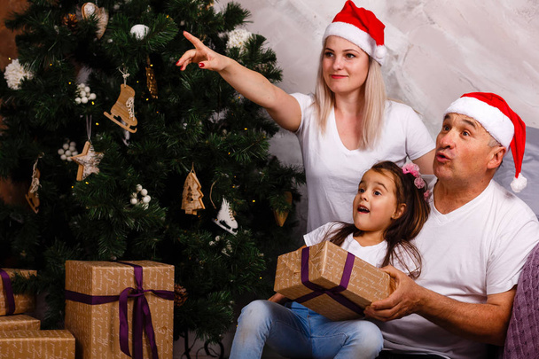 elderly man in Santa hat spending time with granddaughter and daughter near Christmas tree - Φωτογραφία, εικόνα