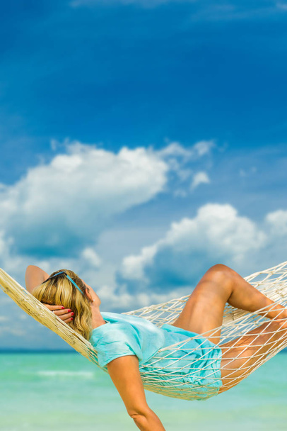 Frau mit Hut sitzt in Hängematte am Strand. Reise- und Urlaubskonzept. - Foto, Bild