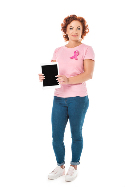 mujer madura con cinta rosa sosteniendo tableta digital con pantalla en blanco y mirando a la cámara aislada en blanco
 - Foto, Imagen