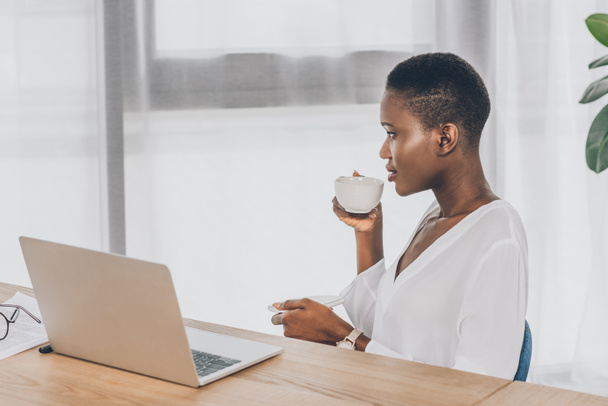 side view of stylish attractive african american businesswoman drinking coffee in office - Fotoğraf, Görsel
