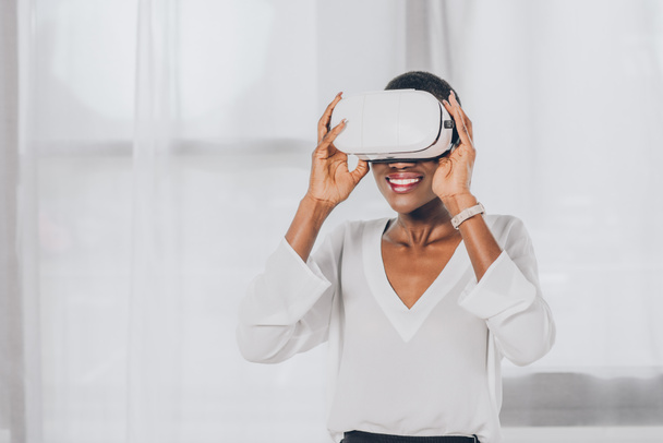 smiling stylish african american businesswoman in virtual reality headset in office - Photo, Image