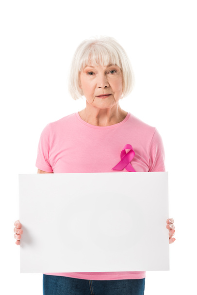 Senior vrouw in roze t-shirt met borst kanker bewustzijn lint leeg banner houden en kijken naar camera geïsoleerd op wit - Foto, afbeelding