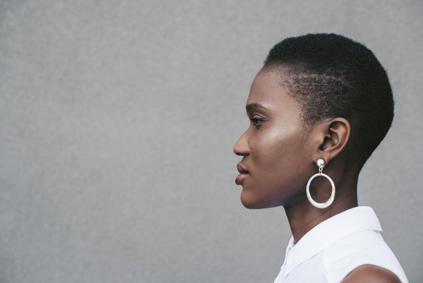side view of stylish attractive african american woman standing near grey wall - Photo, Image