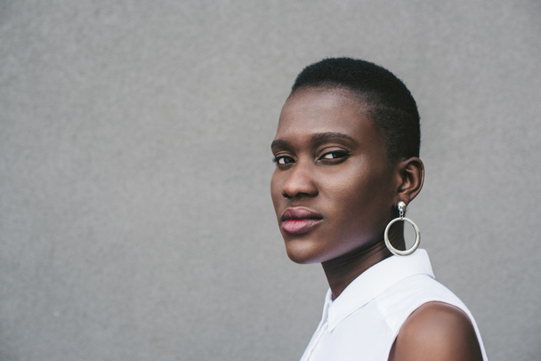 stylish attractive african american woman looking at camera near grey wall - 写真・画像