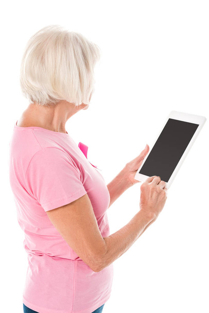 Senior vrouw in roze t-shirt met borst kanker bewustzijn lint met behulp van digitale tablet met leeg scherm geïsoleerd op wit  - Foto, afbeelding