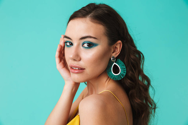 Photo of gorgeous woman 20s wearing fashion makeup and earrings looking at camera isolated over blue background - Fotografie, Obrázek
