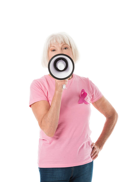 ανώτερων γυναίκα σε ροζ μπλουζάκι με μαστού Καρκίνος κορδέλα ευαισθητοποίησης κρατώντας τηλεβόα και βλέπουν τα φωτογραφικών μηχανών που απομονώνονται σε λευκό - Φωτογραφία, εικόνα